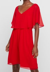 Robe rouge en tissu léger, avec un décolleté en V, des manches volantées et une taille élastique, offrant une coupe décontractée et une silhouette fluide.