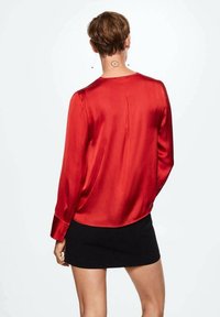 Rode satijnen blouse met lange mouwen, een ronde halslijn en een achterkant met een plooi, gecombineerd met een korte zwarte rok. Glad textuur, glanzende afwerking.