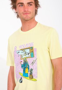 Camiseta de algodón amarilla con un estampado gráfico colorido que presenta un tiburón, un personaje en una tabla de surf y una piña sobre un fondo a cuadriculado.