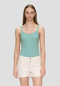 Minzgrüner, gerippter Bodysuit mit dünnen Trägern, kombiniert mit hellbeigen, hochgekrempelten Shorts mit zwei Vorderaschen und einem Knopfverschluss.