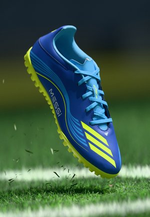 Blue and neon green soccer shoe features a streamlined design, synthetic upper, prominent stripes, and patterned sole with rubber studs.