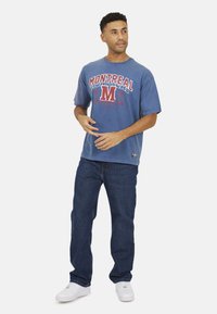Blauwe katoenen t-shirt met de opdruk "MONTREAL" in rood en wit, gecombineerd met donkerblauwe jeans en witte sneakers. Casual fit met korte mouwen.