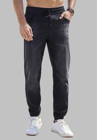 Pantalones jogger de mezclilla negra con cintura elástica, cierre de cordón, bolsillos laterales y tobillos ajustados, combinados con zapatillas blancas.