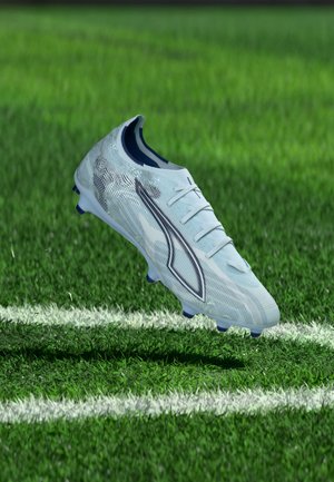 White soccer cleat with dark logo hovering above green grass field near white boundary line.