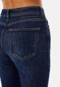Mörkblå denimjeans med en kroppsnära passform, som har en bakficka accentuerad med röd sömnad och kontrasterande gula sömmar.