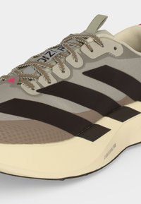 Μπεζ και καφέ ελαφρύ παπούτσι για τρέξιμο με υφή στη μύτη, ριγωτό σχέδιο στο πλάι και επώνυμο μαλακό πέλμα με την ένδειξη "Lightstrike Pro."