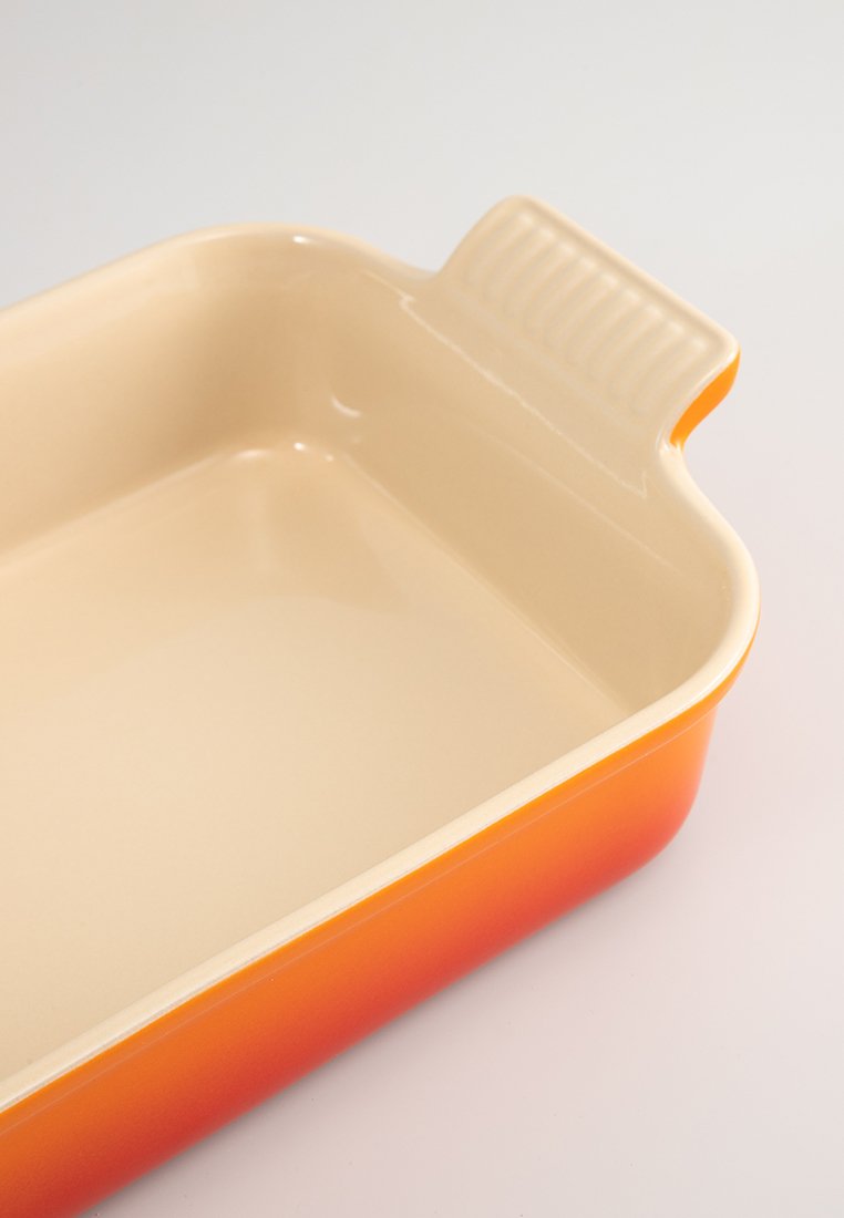 Rechteckige Keramikbackform mit glattem, beigen Innenraum und orangefarbigem Farbverlauf im Außenbereich. Verfügt über einen gerillten Griff für einen sicheren Halt.