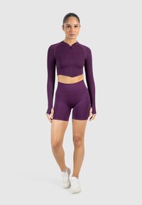 Lilla cropped jakke med fuld lynlås og lange ærmer, parret med højtaljede shorts. Glat, strækbart stof, tætsiddende design.