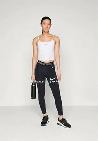 Black Nike Pro leggings with white logo, fitted white crop top, holding a black water bottle, completed with black athletic shoes.