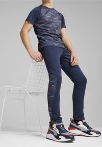 Marinblå atletisk T-shirt med vågmönster, matchad med åtsittande marinblå byxor med röda detaljer. Svarta, röda och vita sneakers fulländar looken.