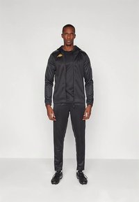 Tuta nera in tessuto liscio; presenta una felpa con cappuccio con cerniera, logo Kappa in oro e design aderente con maniche lunghe e pantaloni con taglio affusolato.