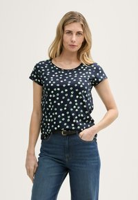 T-shirt bleu marine à manches courtes avec des pois verts, col rond et coupe décontractée, associé à un jean bleu et une ceinture noire.