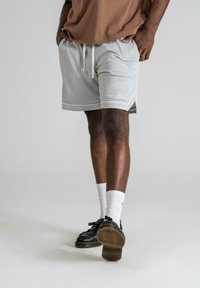 Light gray mesh shorts with a drawstring waist and side pockets, featuring white trim and a logo on the hem, worn with black shoes and white socks.