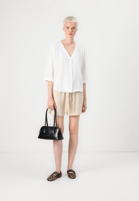 White button-up blouse with three-quarter sleeves, beige shorts, black handbag, and patterned loafers with a leopard print.