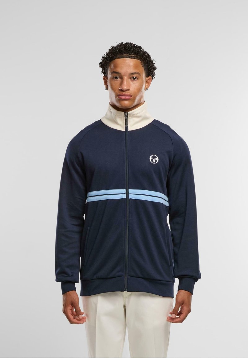 Mornarska zip-up jakna z visokim ovratnikom in svetloblue akcentnimi črtami. Ima majhen logo na prsih ter rebraste manšete in rob.