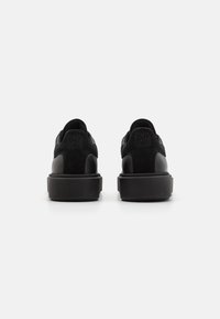 Sneaker nere con tomaia in suede e pelle, caratterizzate da una suola spessa e testurizzata. La parte posteriore include una patch con logo e un design del tallone arrotondato.