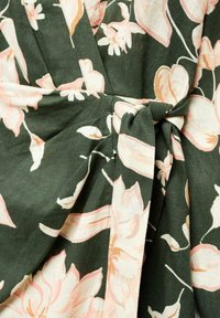 Un tissu floral vert avec des fleurs roses et crème, doté d'un détail de taille nouée. La texture semble douce, avec une finition légèrement froissée.