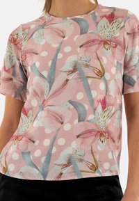 Top a maniche corte in tessuto rosa chiaro con stampa floreale in tonalità di rosa, blu e arancione, e pois bianchi distribuiti su tutto il capo.