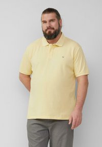 Polo-Shirt in hellgelb, aus strukturiertem Stoff. Mit einem klassischen Kragen und einem kleinen, auf der Brust gestickten Logo.