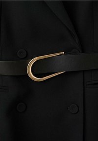 Blazer noir croisé à double boutonnage avec des boutons recouverts de tissu, cintré à la taille par une ceinture en cuir noir avec une boucle dorée en forme de U.