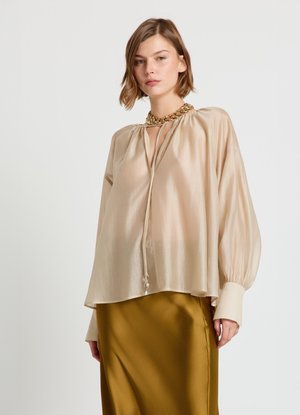 Blouse en soie beige avec encolure goutte d'eau, détail froncé et manches longues et amples ; associée à une jupe lisse en satin vert olive.