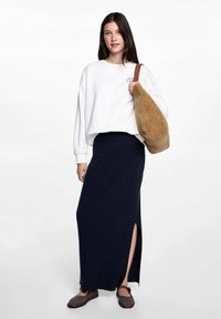 Bílý oversized svetr, námořnická pletená maxi sukně s bočním rozparkem, hnědá nubuková taška přes rameno a tkané slip-on boty.