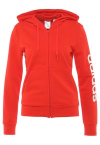 Felpa rossa con zip realizzata in misto cotone, con tasca frontale, cappuccio regolabile con cordino e logo Adidas bianco lungo la manica.