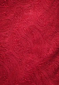 Rood gestippeld stof met wervelende ontwerpen en een gestructureerd oppervlak, wat een verhoogde en tastbare kwaliteit biedt.