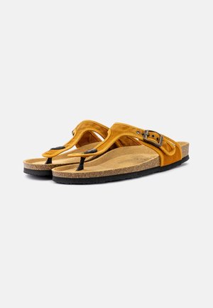 Sandalias de ante amarillo con una plantilla de corcho, suela de goma negra y una hebilla de acento negra. Diseñadas en estilo de dedo.