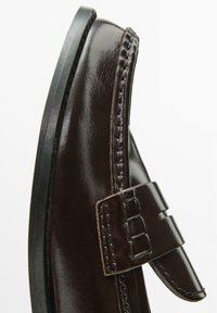 Scarpa in pelle marrone con finitura liscia, forma arrotondata e dettagli decorativi con cuciture. Presenta una cintura sicura con dettaglio della fibbia.
