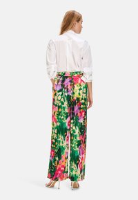 Fließende, farbenfrohe Blumenhose mit einem lebhaften Muster aus Pink, Lila und Grün, kombiniert mit einem schicken weißen Hemd mit Kragen.