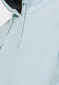 Sudadera con capucha azul claro hecha de tela suave, con capucha ajustable mediante cordón y ojetes plateados, con textura suave y detalles mínimos.