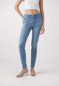 Ljust blå denimjeans med slim fit, klassisk femficksdesign och subtila sömnadsdetaljer. Matchas med vita klacksandaler.