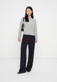 Maglia grigia a maniche lunghe abbinata a pantaloni larghi blu navy, con vestibilità rilassata e texture morbida. Include una piccola borsa nera.