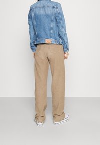 Blue denim jacket with a back patch, paired with tan corduroy wide-leg pants and white sneakers, viewed from the back.