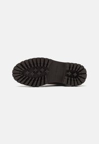 Semelle d'une botte noire avec des motifs de semelle profonds et le nom de la marque « Tommy Hilfiger » embossé sur la zone de la voûte plantaire.