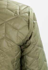 Quilted olive green jacket featuring a hexagonal pattern, smooth sheen, padded texture, and structured shoulder design.