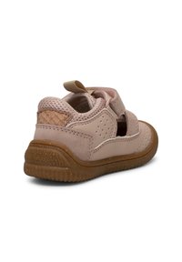 Chaussure pour tout-petit rose clair avec côtés perforés, patte de talon texturée, bride en velcro et semelle en caoutchouc marron, vue de l'arrière en angle latéral.