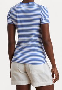 Modro-bílá pruhovaná košile s krátkým rukávem a kulatým výstřihem, vyrobená z měkkého materiálu, spárovaná s světle béžovými lněnými kraťasy.