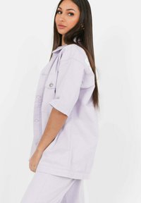 Lila oversized jeansjacka med korta ärmar, framfickor och silverfärgade tryckknappar, bärs med matchande underdel.