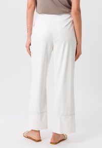 Witte wijde broek met een gladde afwerking, voorzien van zijnaad en een zoomdetail. Gecombineerd met tan kleurige instapsandalen.