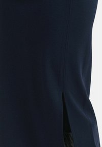 Navyblaues Kleid mit glatter Textur, seitlichen Schlitzen für Bewegungsfreiheit und einer figurbetonten Silhouette ohne sichtbare Verschlüsse.