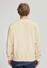 Felpa in cotone crema con scollo rotondo, polsini e orlo a coste, dalla texture liscia e dal fit rilassato. Vista posteriore mostrata.