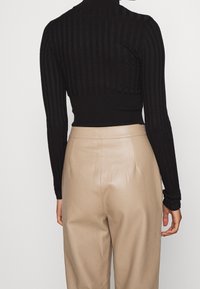 Haut noir à manches longues côtelé avec un col montant, associé à un pantalon en cuir beige taille haute, mettant en valeur une texture lisse et une coupe ajustée.