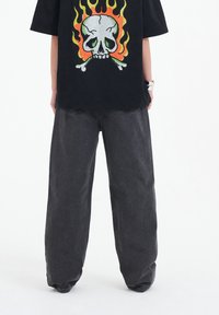 Svart oversized t-shirt med en flerfärgad dödskalle och flamor tryck, kombinerad med lössittande mörkgrå denimjeans.