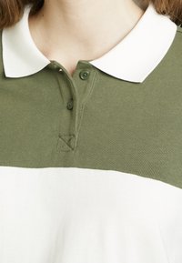 Gros plan sur un polo vert et blanc avec col, deux boutons fermés au niveau du haut de la poitrine et du cou d'une personne.