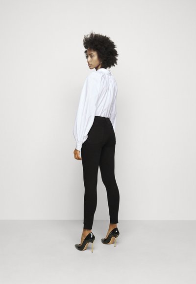 Crne skinny traperice visokog struka uparene s bijelom bluzom dugih rukava. Model nosi crne štikle s metalnim detaljem.
