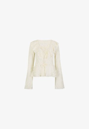 Blusa in pizzo crema con maniche lunghe a campana, scollo arricciato, vita peplum e fiocchi decorativi sul davanti.