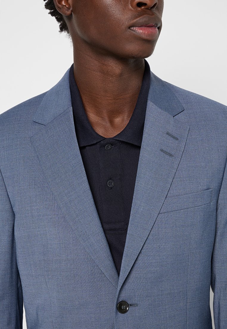 Hellblaues Blazer aus strukturiertem Stoff, mit einem Knopfverschluss und drei vertikalen Nahtdetails. Kombiniert mit einem dunkelblauen Poloshirt darunter.