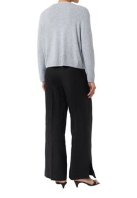 Helles graues, kurz geschnittenes Strickpullover mit geripptem Saum; kombiniert mit schwarzen, weit geschnittenen Hosen mit seitlichen Schlitzen; Model trägt offene Schuhe mit Absatz.